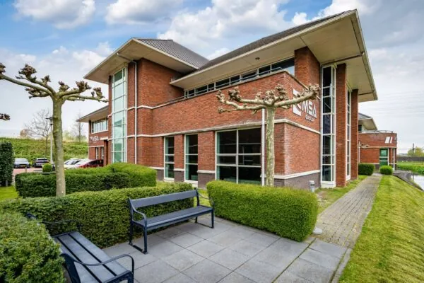 Modern kantoorpand aan de 1e Barendrechtseweg met rode bakstenen gevel, grote ramen en verzorgde groenvoorziening.